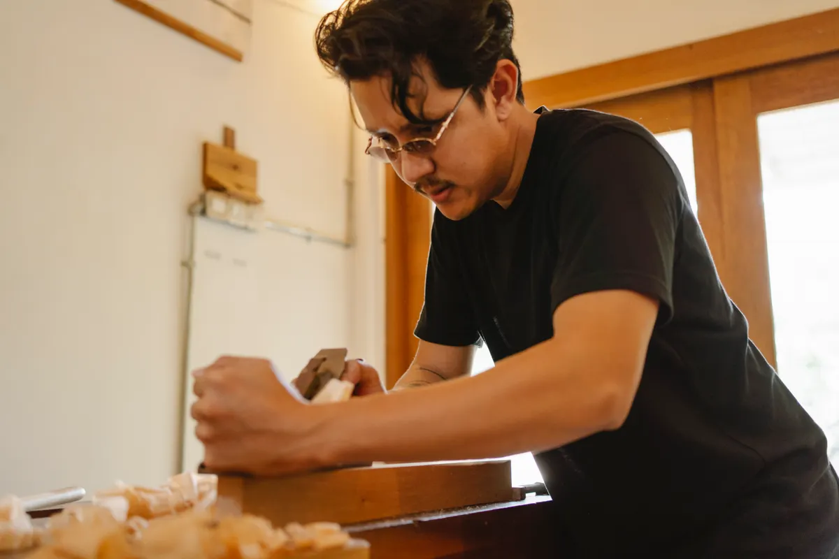 A beginner wood carver carefully working on a small block of soft basswood at a workbench.