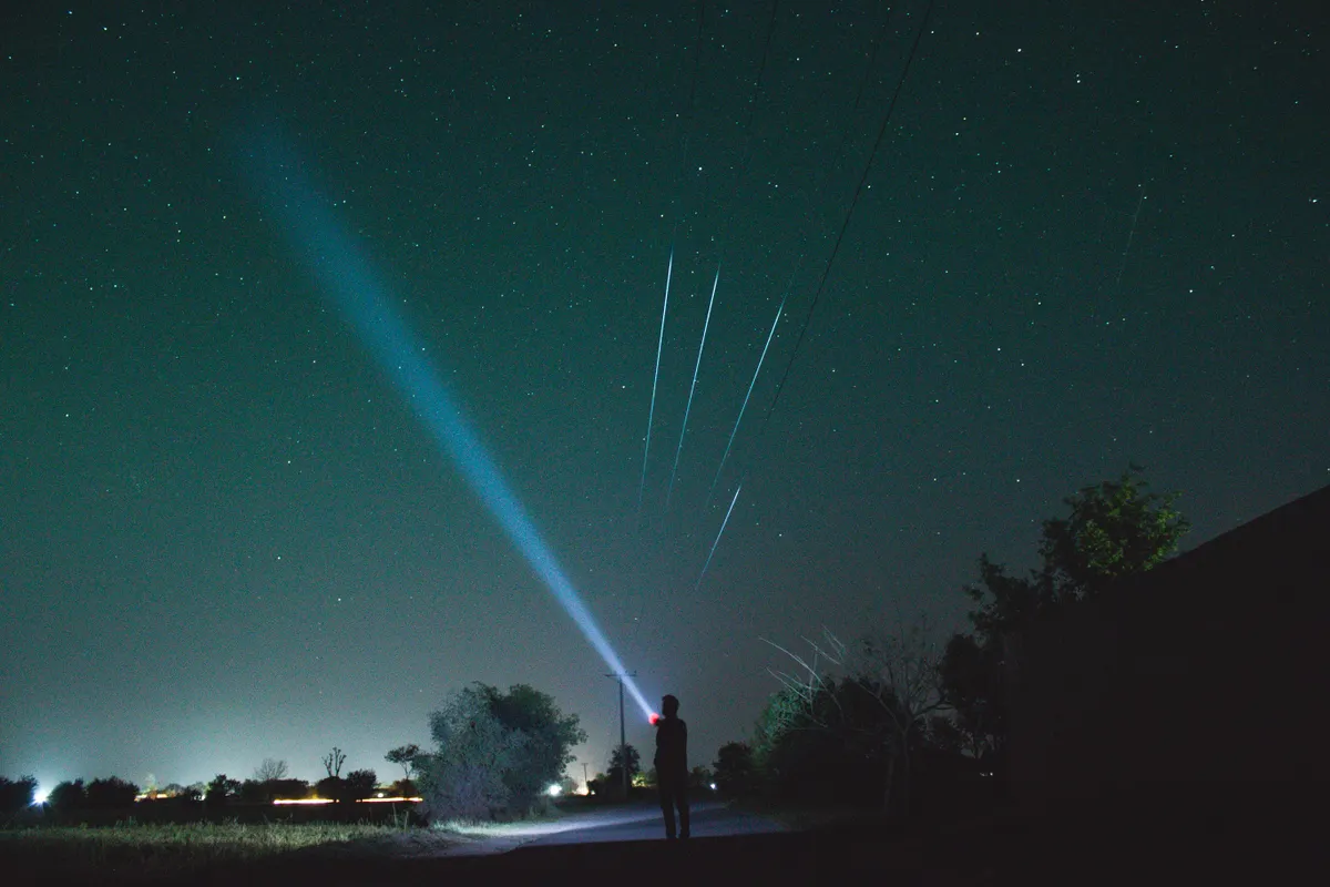 A stargazer using a handheld red LED flashlight to examine equipment under a night sky