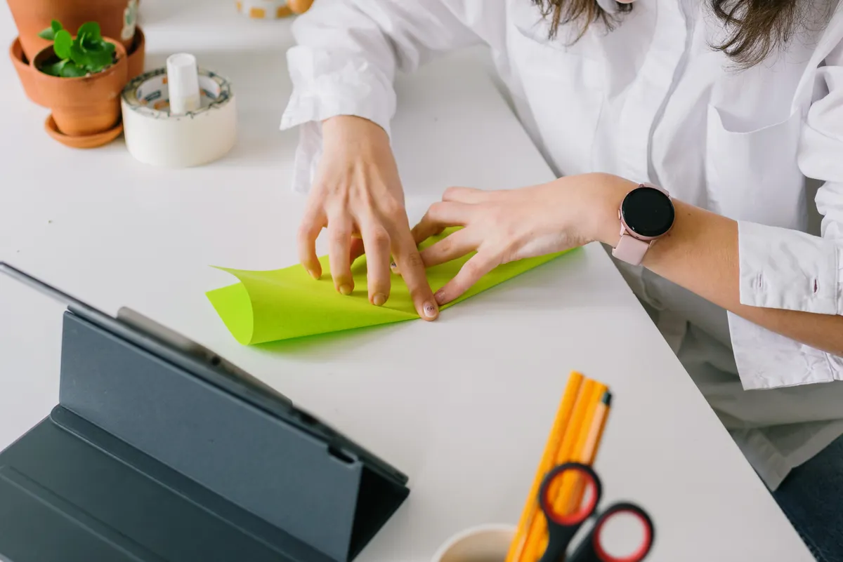 A pair of hands carefully folding a crisp square of paper into a three-dimensional crane.