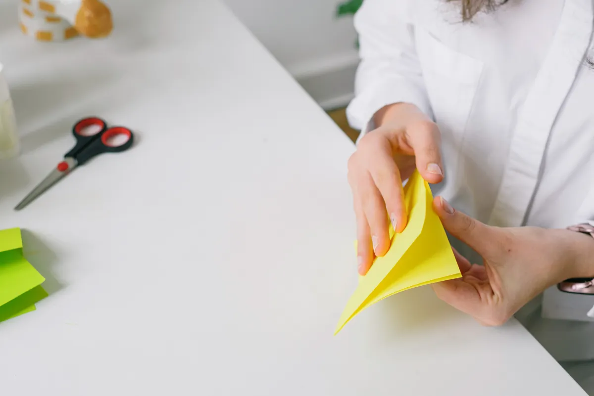 Hands practicing core beginner origami folds on crisp square sheets of paper.