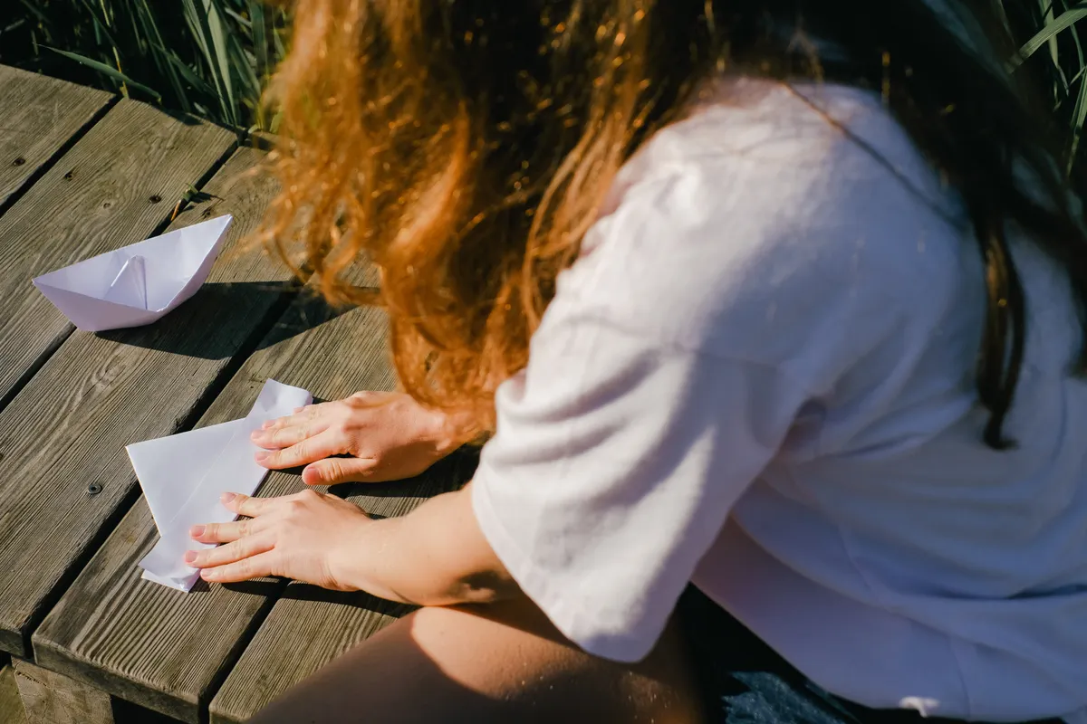 A beginner successfully creating a simple origami fold on a flat wooden desk.
