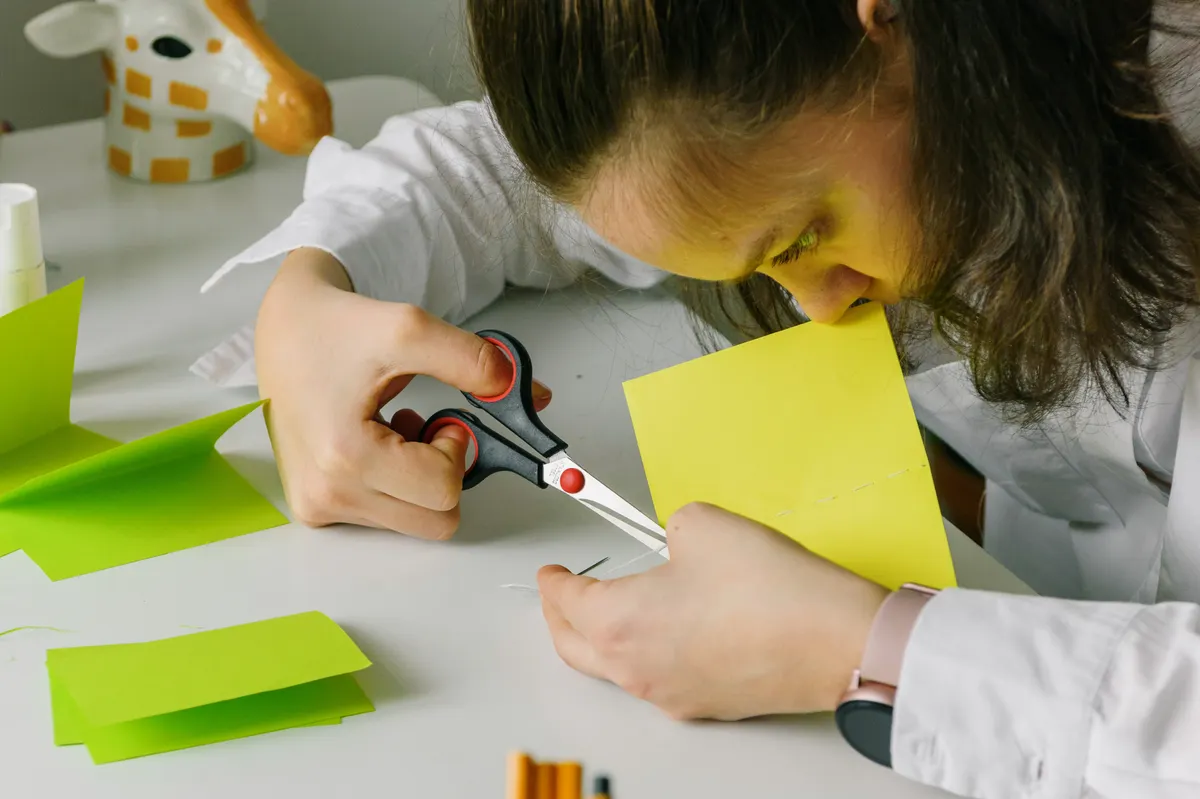 Hands carefully using precision scissors to cut along the folded edges of a patterned paper sheet.