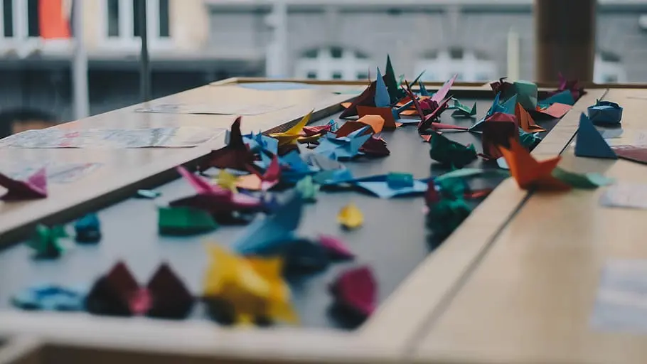 Hands carefully threading a needle through multiple folded paper cranes for a senbazuru string.