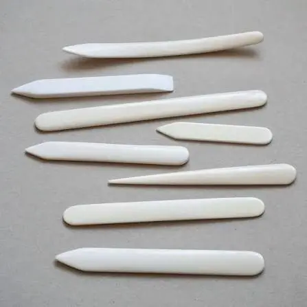 A smooth bone folder tool resting beside a crisp paper crease on a flat workspace.