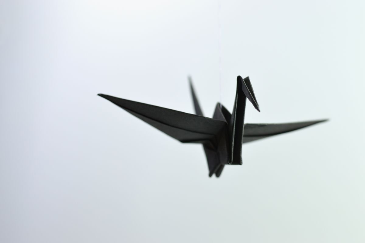 A crisp white paper crane resting on a neutral wooden tabletop surface.