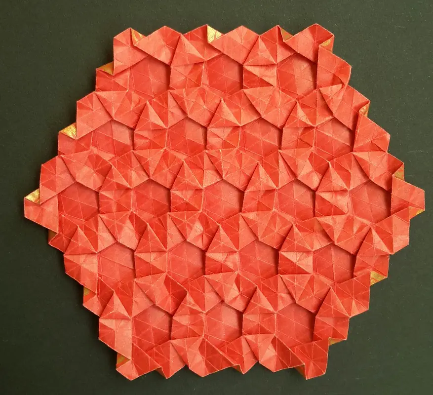A hand pressing and twisting a paper hexagon to create raised textured sections in origami.