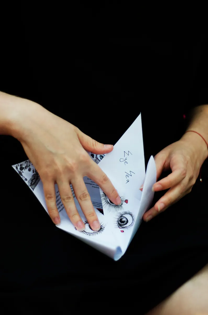 Hands carefully unfolding layers of paper to reveal a pre-creased point for an open sink fold.