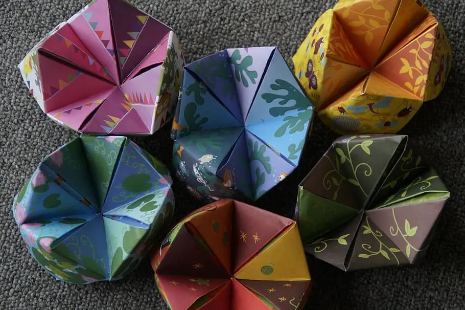 Close-up of hands working through a multi-step paper folding diagram at a table.