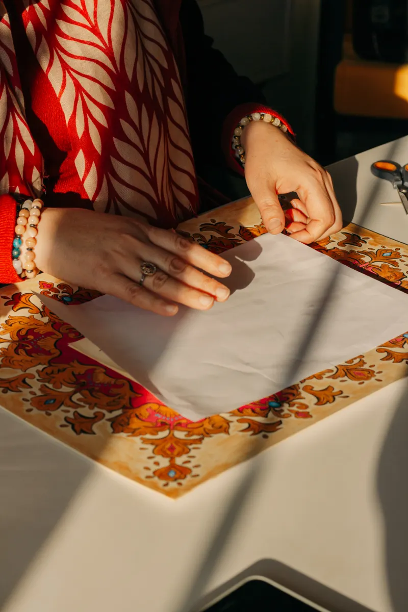 Hands folding a square sheet of paper toward the center to create a valley crease.