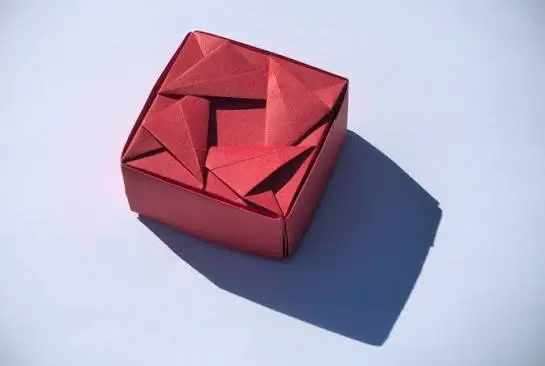 A small handcrafted paper box holding light desk items like paperclips and small supplies.