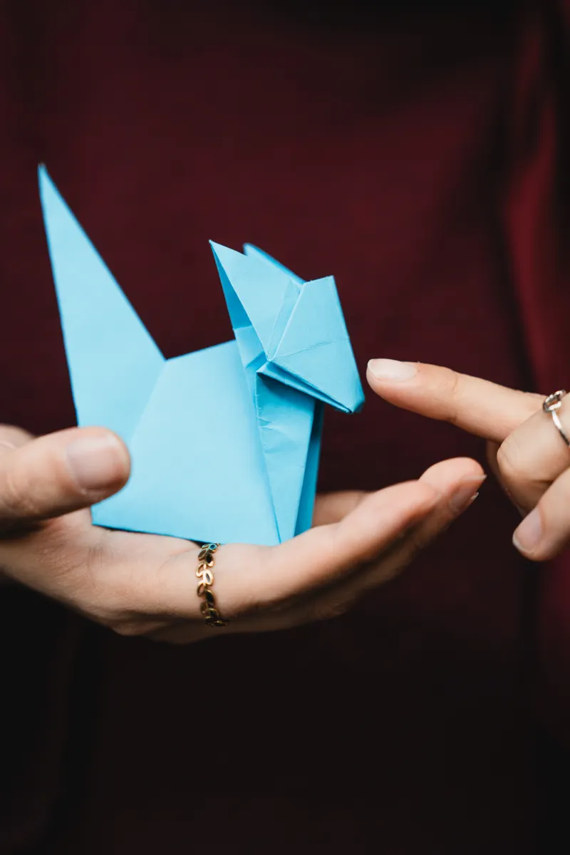 A square sheet of paper being folded without scissors or glue to demonstrate true origami basics.